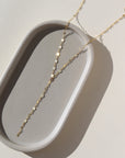 14k gold fill Sylvie Lariat laid on a gray plate in the sunlight.