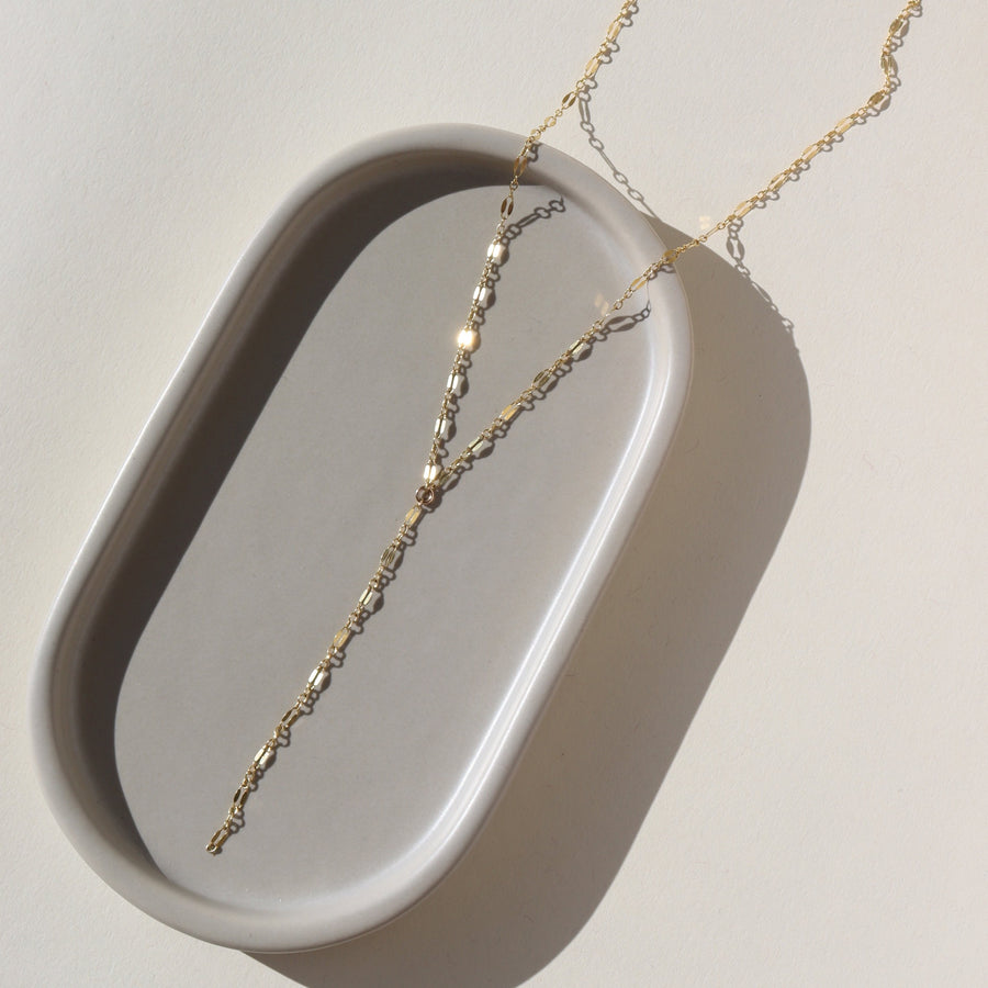 14k gold fill Sylvie Lariat laid on a gray plate in the sunlight.