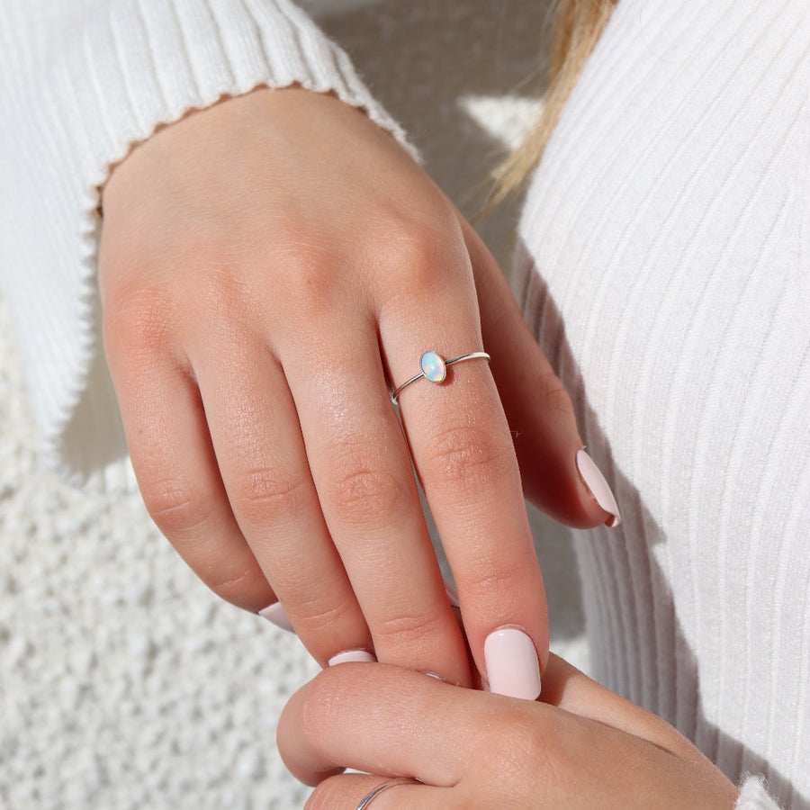 Model wearing 925 Sterling silver Opal Essence Ring laid on pointer finger. This ring features a smooth band with  oval opal. These pair great with our stacking rings.
