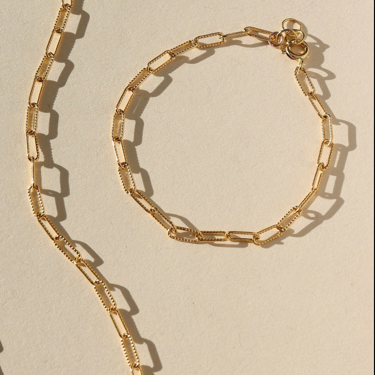Gold chain necklace and bracelet on a beige background