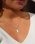 Model wearing 14k gold fill Everly Charm necklace. This necklace feature a simple chain with a box charm and the charm has hammering on the outside, Laid on top of the box charm is a opal stone.