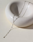 sterling silver lariat chain, photographed on a cream colored ceramic dish