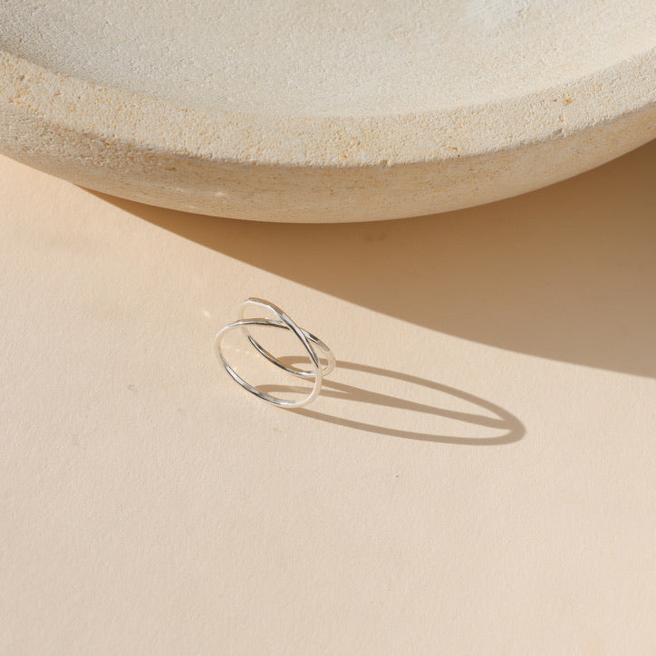 sterling silver hammered ring that crosses itself on a light background