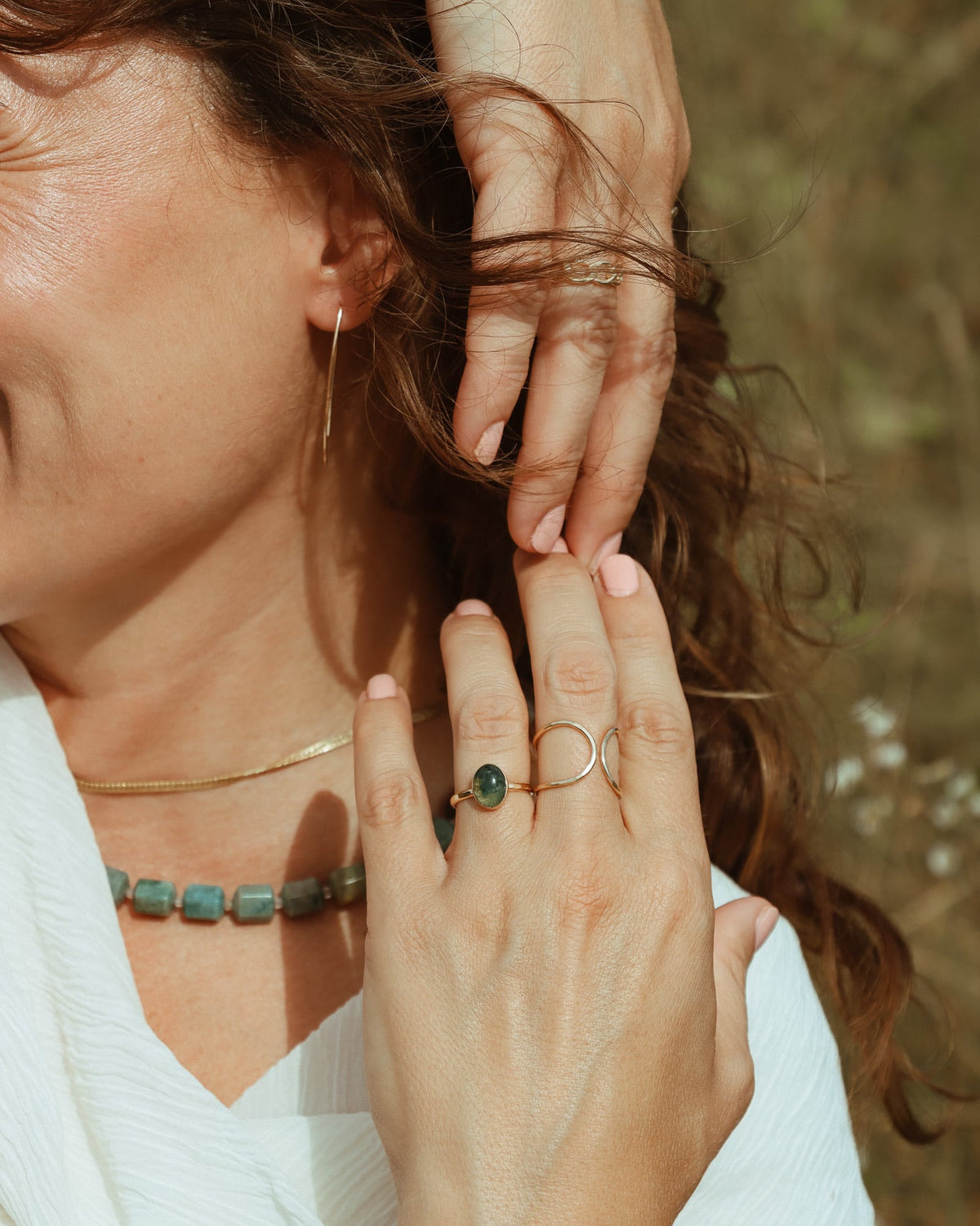 Woman wearing a hammered gold hoop earring with layered gold ear cuffs and delicate chain details.