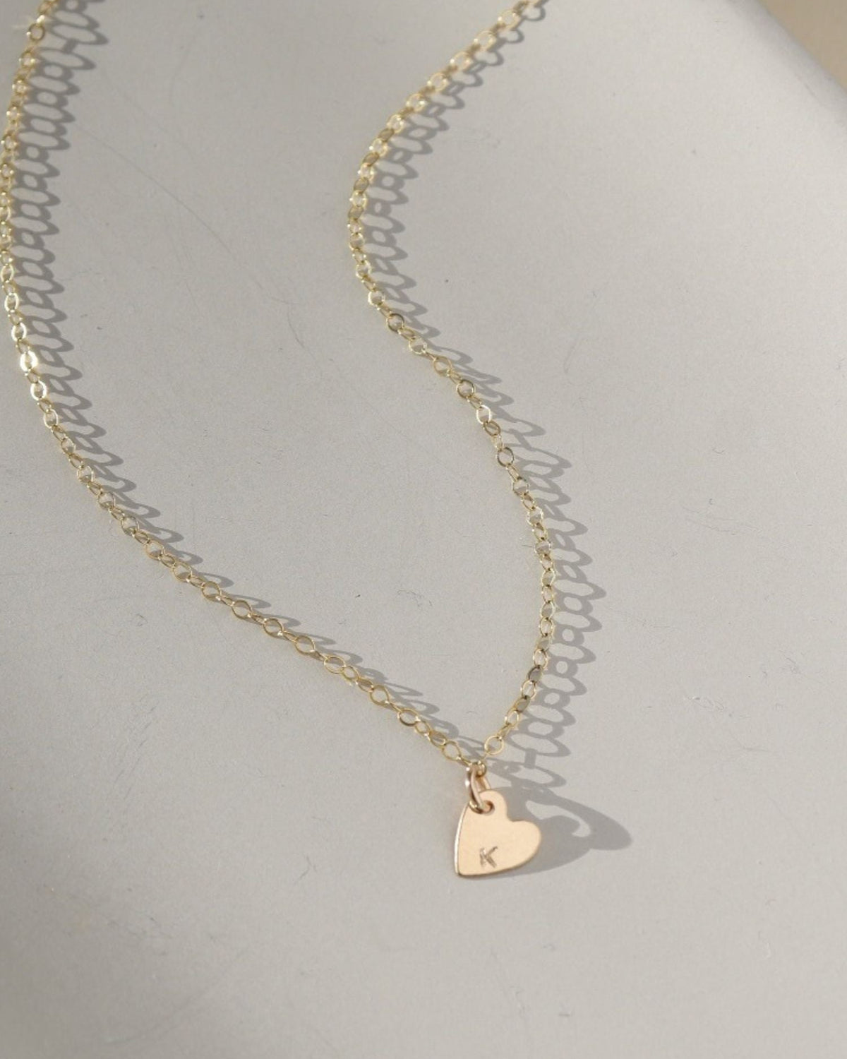 a dainty heart charm with an initial stamped on them, on a necklace chain, photographed on a ceramic dish