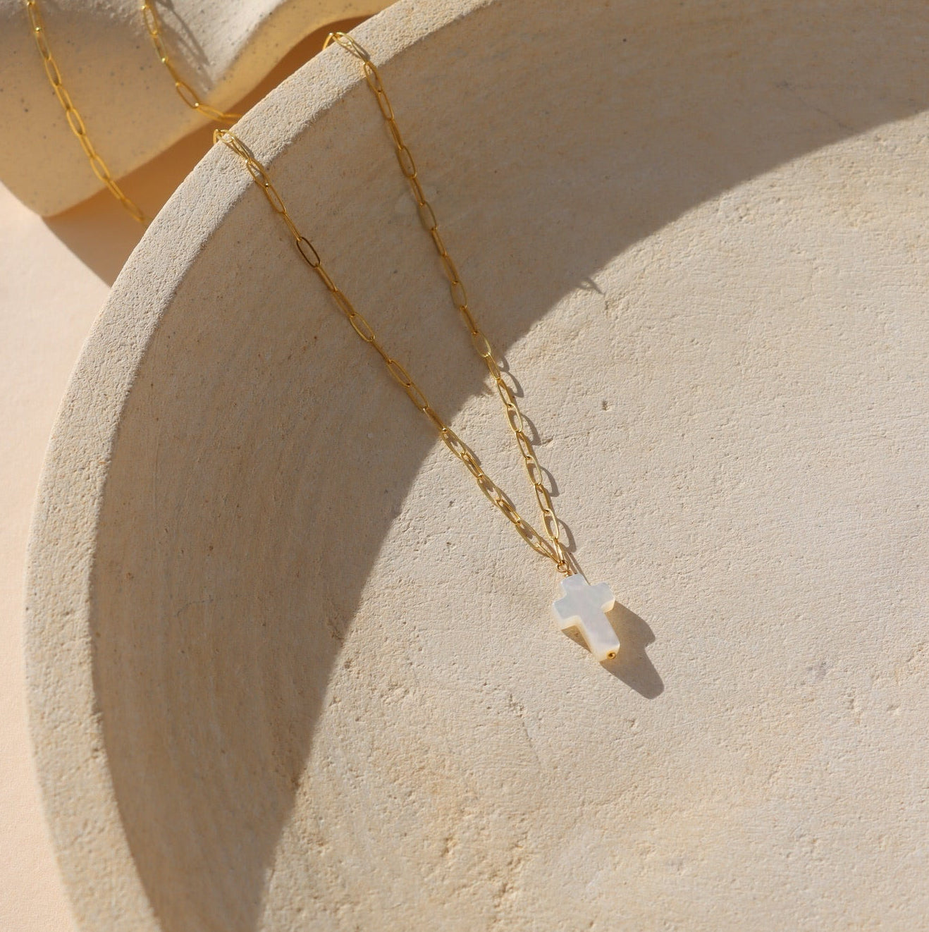 14k gold fill paperclip chain with a mother of pearl cross bead pendant on a light plate