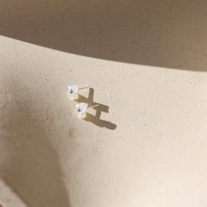 Pair of mother-of-pearl flower stud earrings with polished sterling silver centers resting on a textured cream ceramic display in warm natural light.