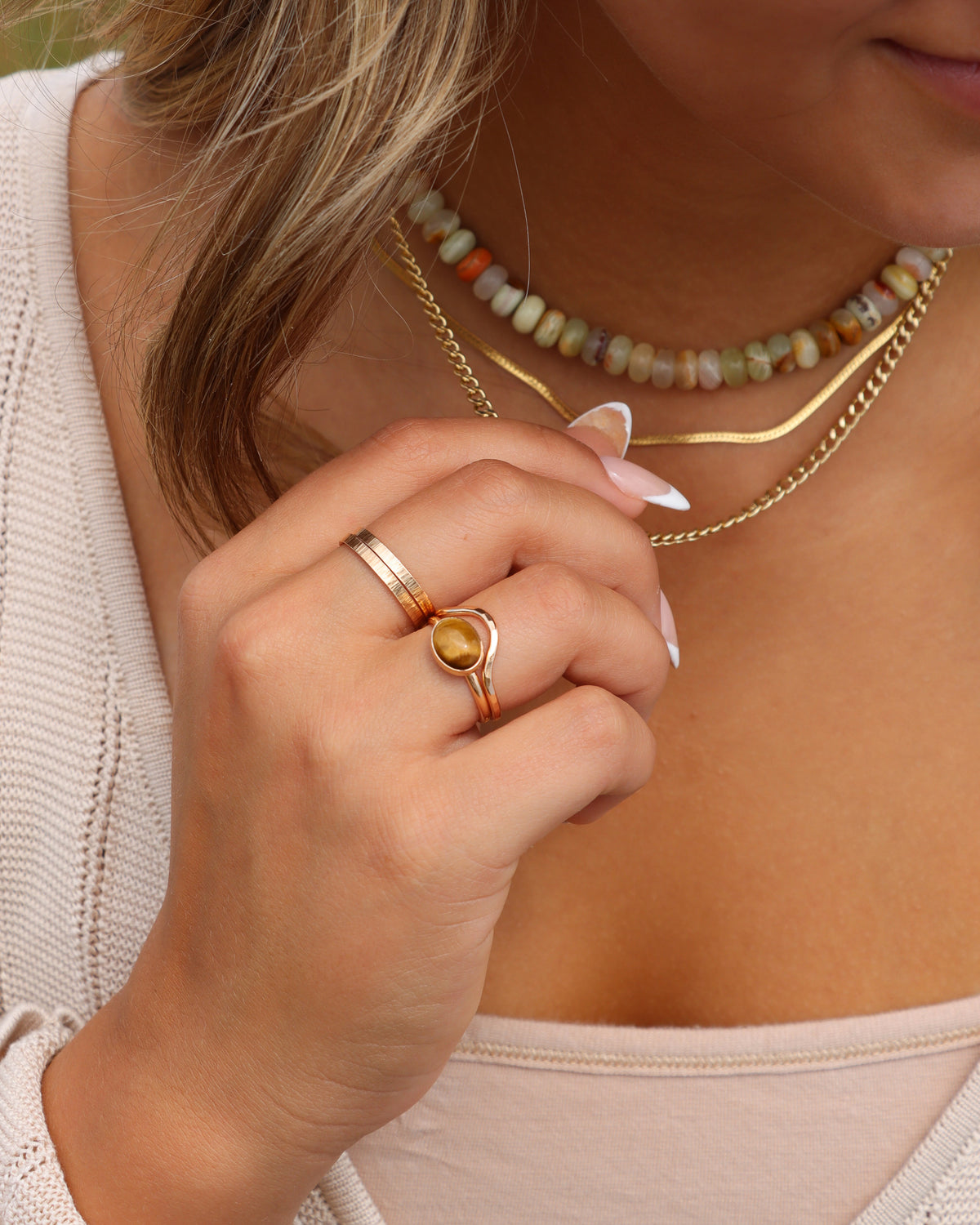 Woman wearing layered gold necklaces and stacked gold rings with a tiger’s eye gemstone ring.