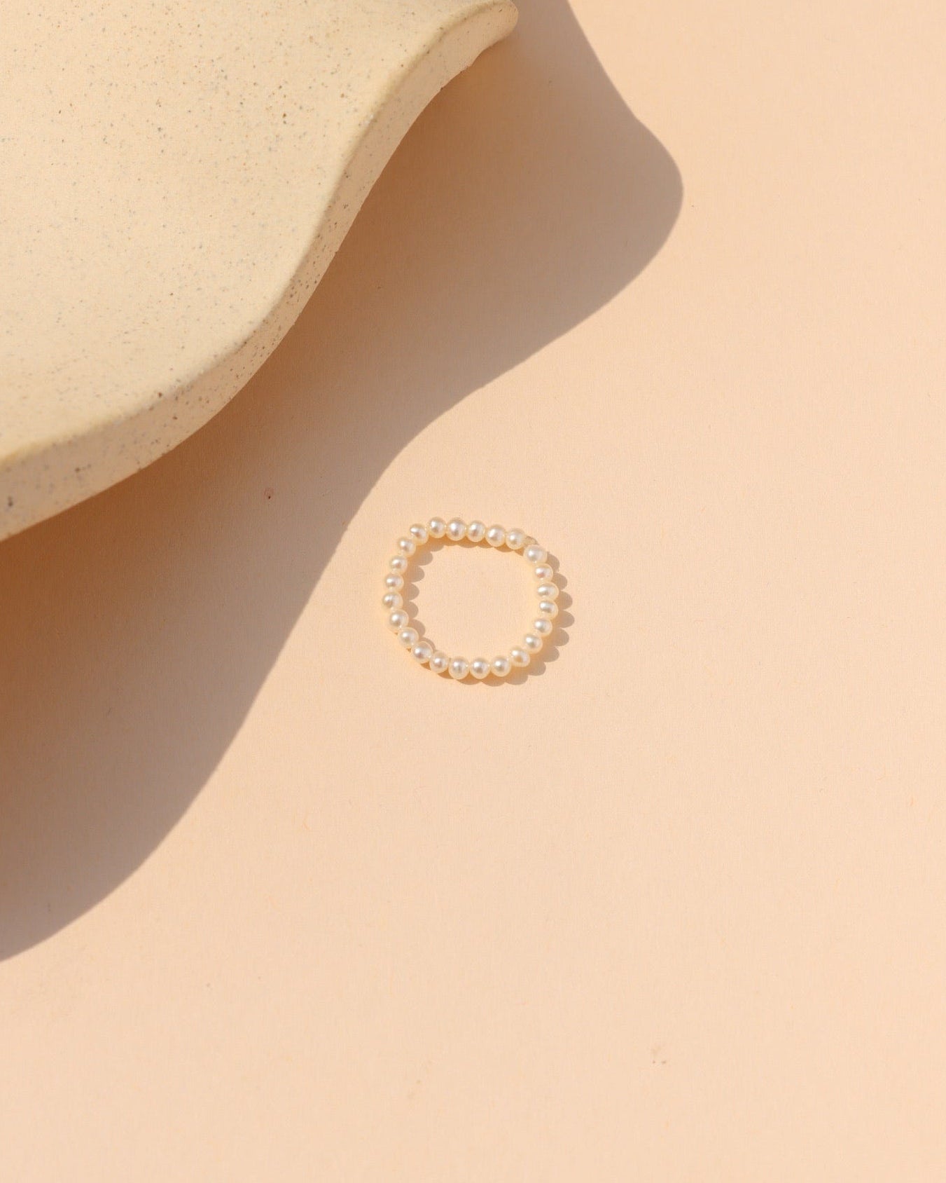 Beaded hand-strung pearl stacking ring laying on a beige surface in the sunlight.