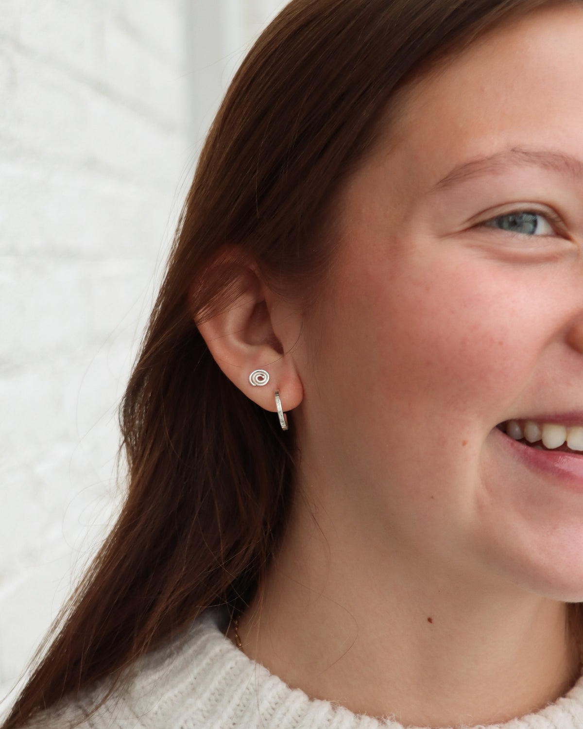 Close-up of a model wearing silver spiral stud earrings paired with small textured sterling silver hoops for a delicate layered ear stack.
