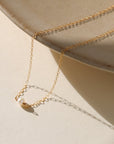 Gold necklace with a small pendant on a beige surface