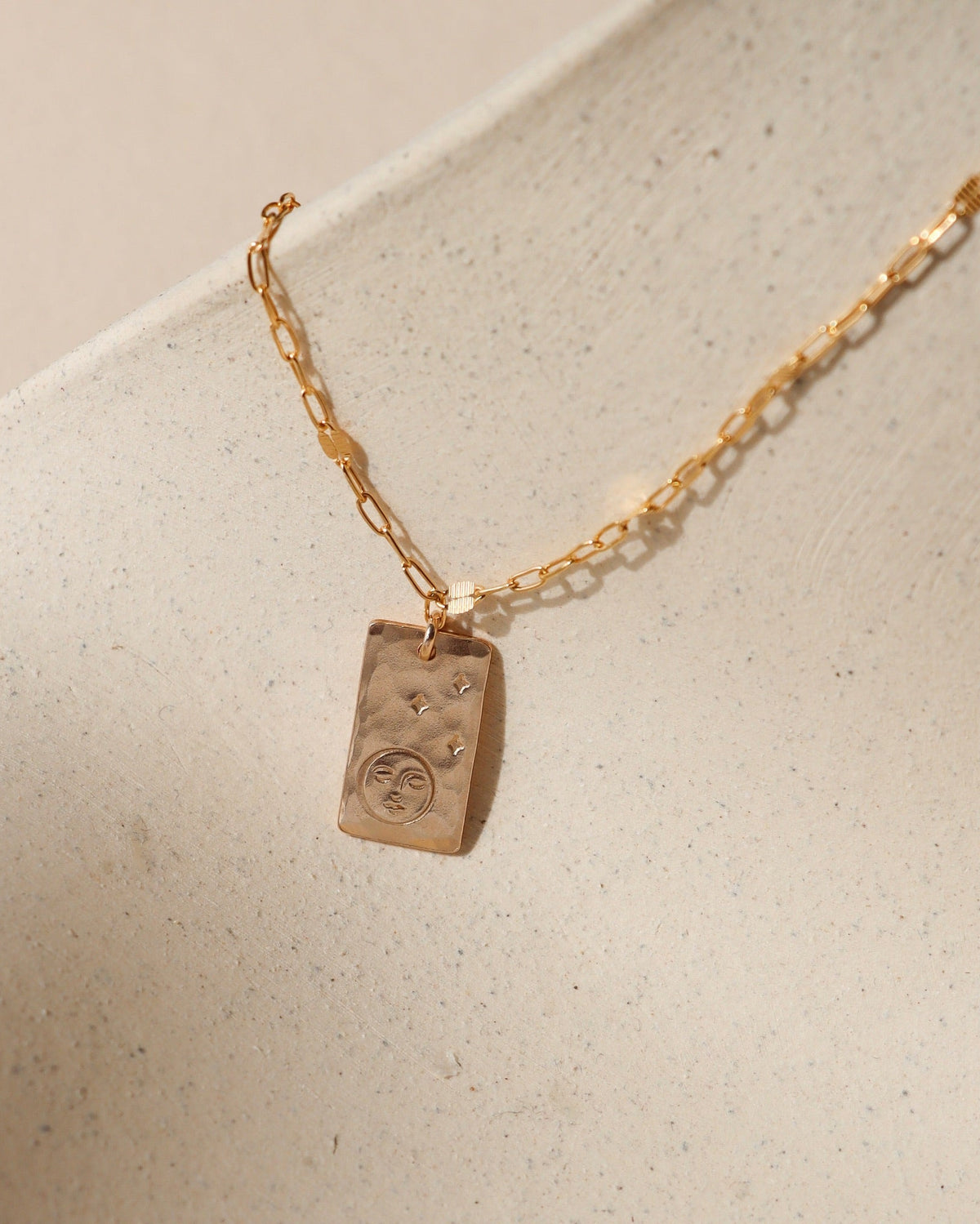 14k gold fill chain necklace with hand stamped moon &amp; stars pendant on a light dish