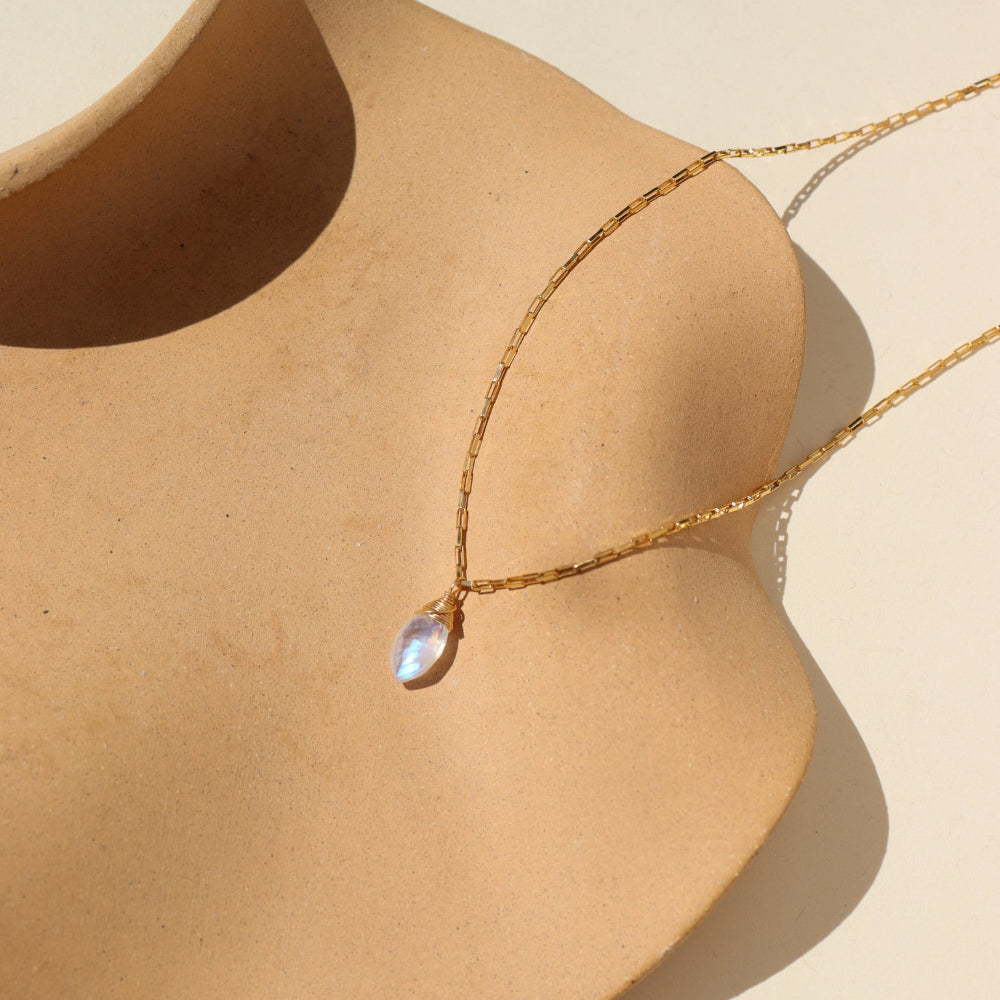 A 14k gold fill box chain featuring a Marquise Moonstone Gemstone wired wrapped at the end. Necklace is displayed on a orange dish. 