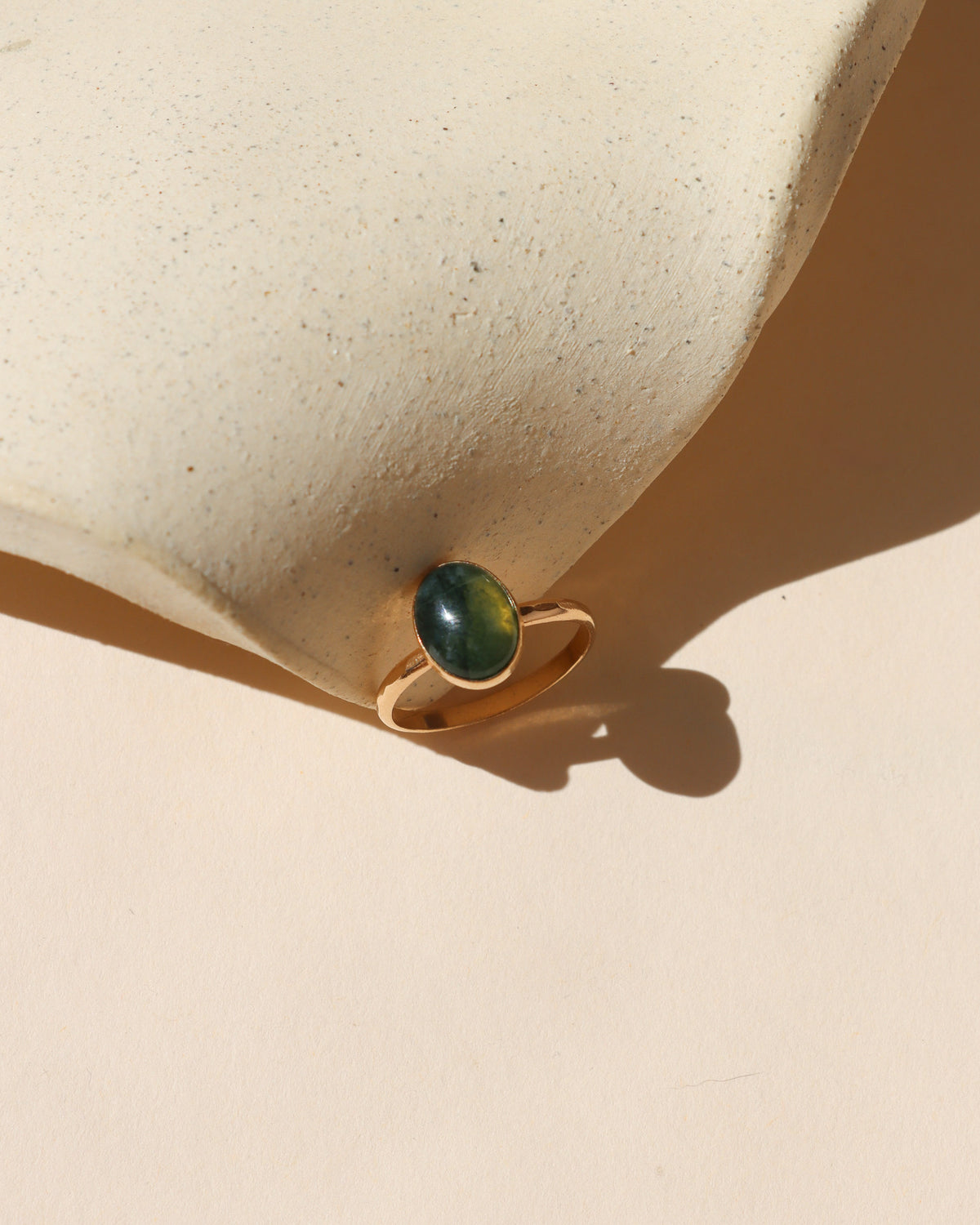 Oval green gemstone ring in a gold setting, displayed in warm sunlight against a neutral background.