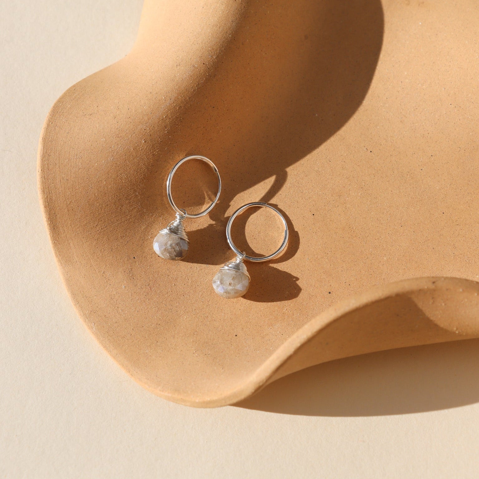 Sterling silver hoop earrings featuring iridescent moonstone charms with soft, shimmering hues.