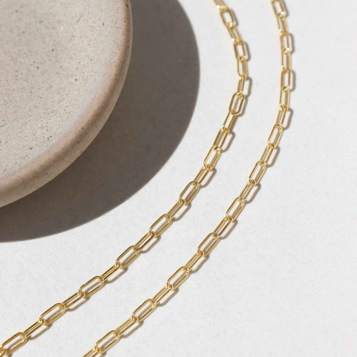 14k Gold fill Narrow Links chain laid on a white paper in the sunlight.