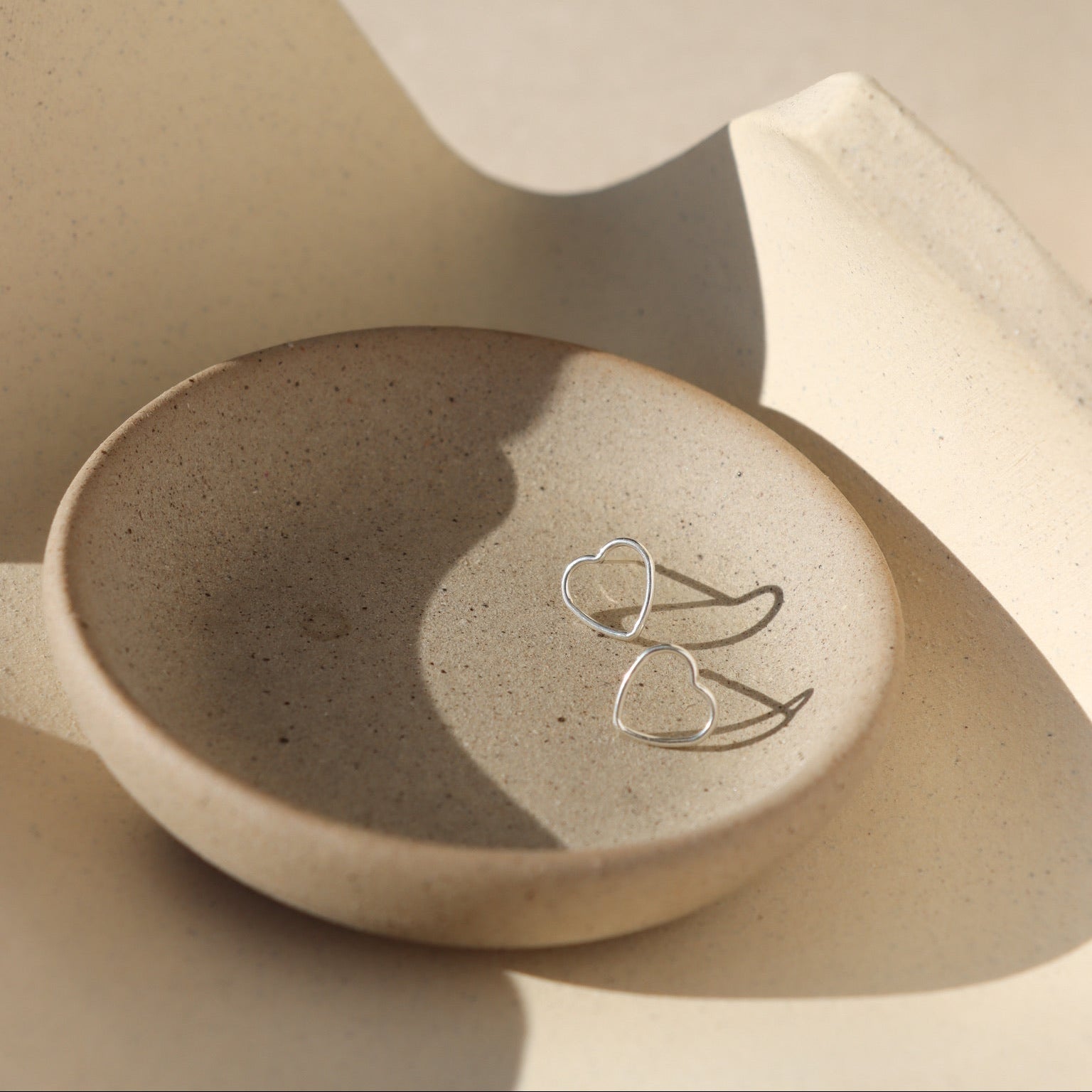 sterling silver open heart stud earrings on a light dish