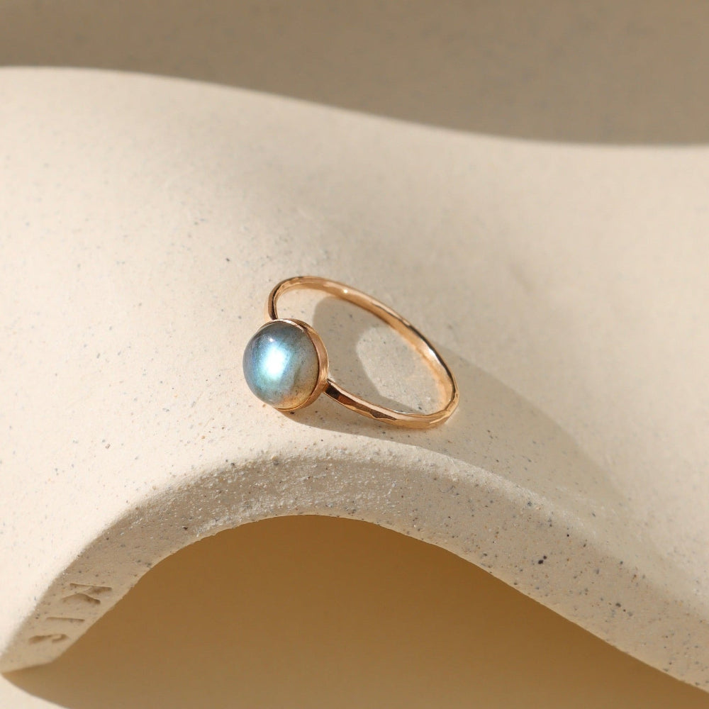 Gold ring with a blue gemstone on a beige stone surface
