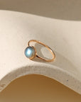 Gold ring with a blue gemstone on a beige stone surface