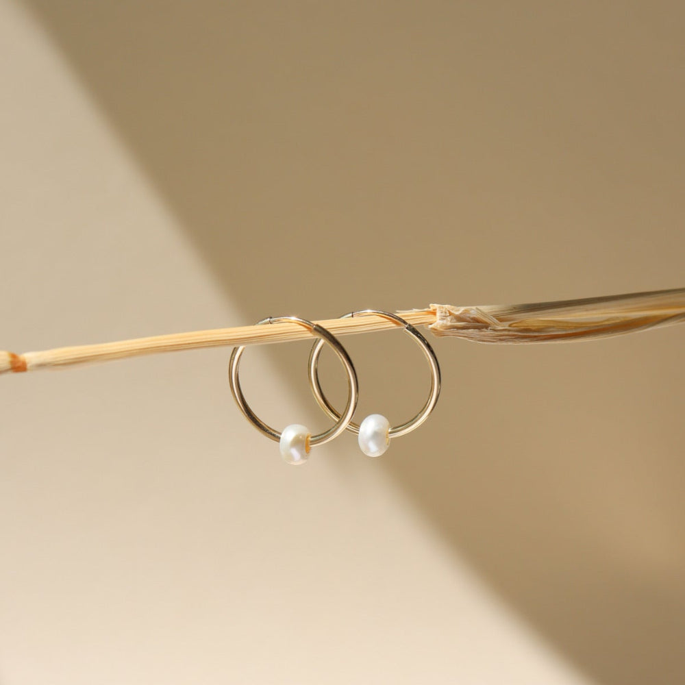 14k gold fill 14mm hoops with a freshwater  pearl dangling from the bottom of each hoop, the earrings are displayed on a post in the sunlight  