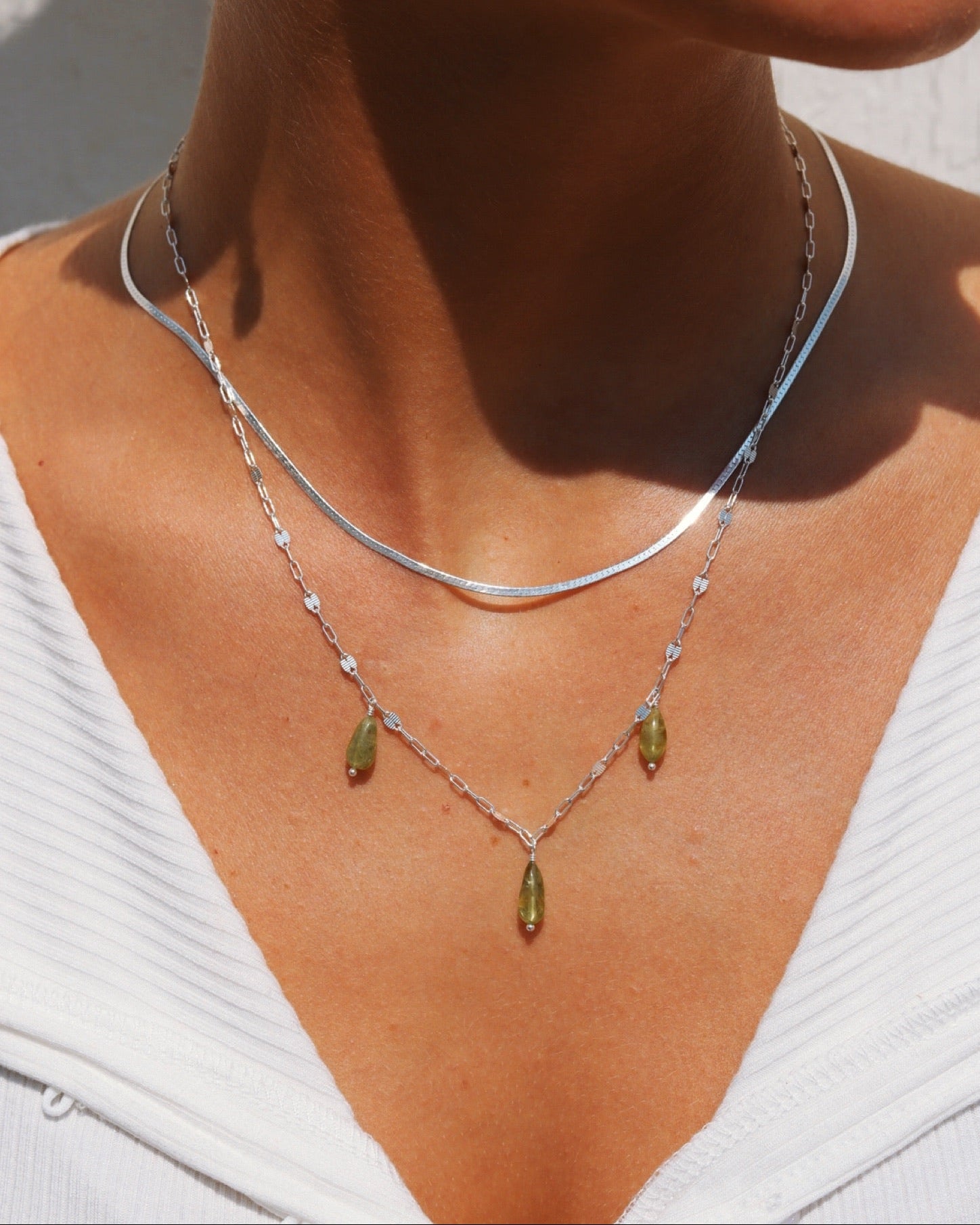 Model wearing a sterling silver Peridot Charm Necklace with three green gemstone drops, layered with a silver herringbone chain.