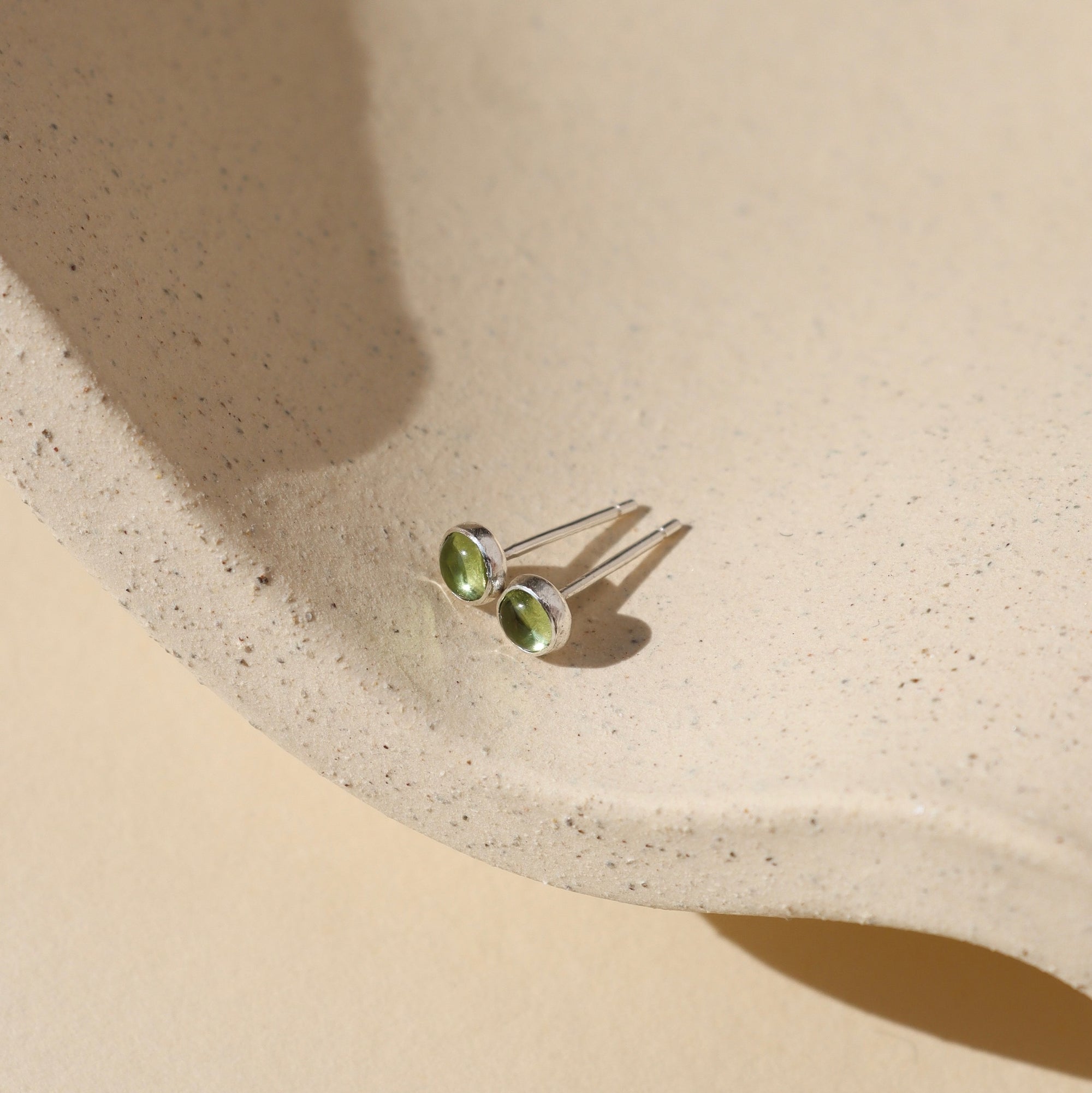 sterling silver ear posts with 4mm peridot stones on a light dish