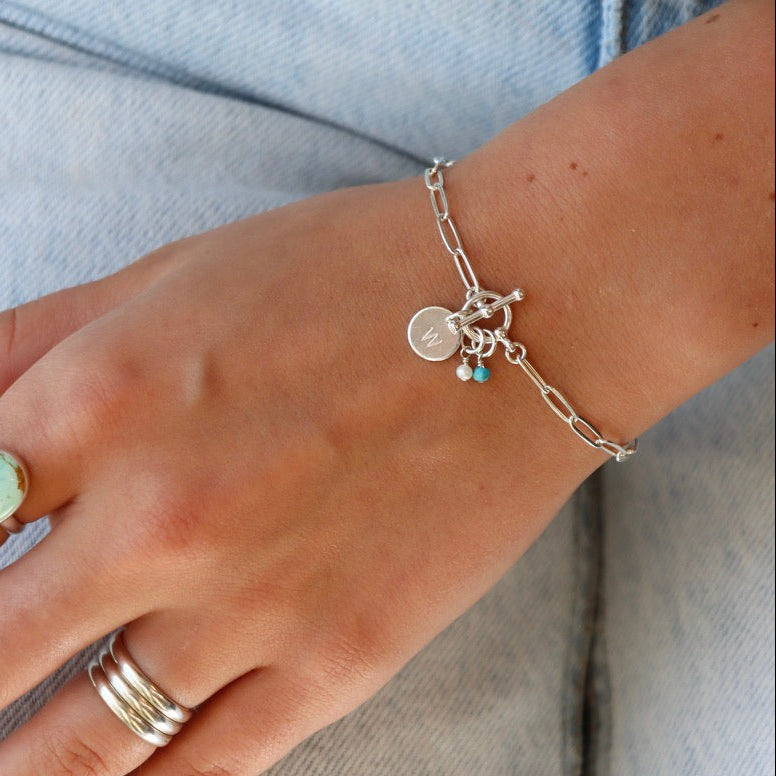 model wearing sterling silver chain bracelet with toggle clasp, birthstone charms, and W disc charm paired with other sterling silver jewelry