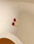 Gold filled bezel set earrings with July's birthstone, red Ruby gemstones on a ceramic dish
