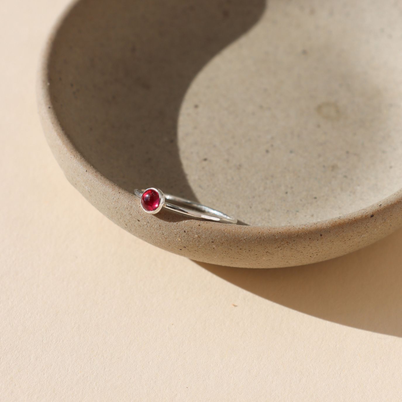 sterling silver bezel ring with 4mm ruby gemstone on a light dish