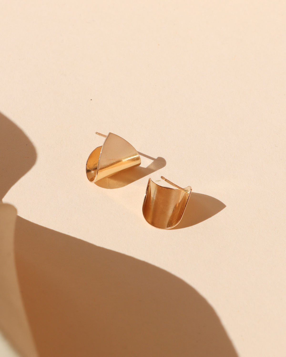 Sculptural gold stud earrings with a polished folded design that catches and reflects the light.
