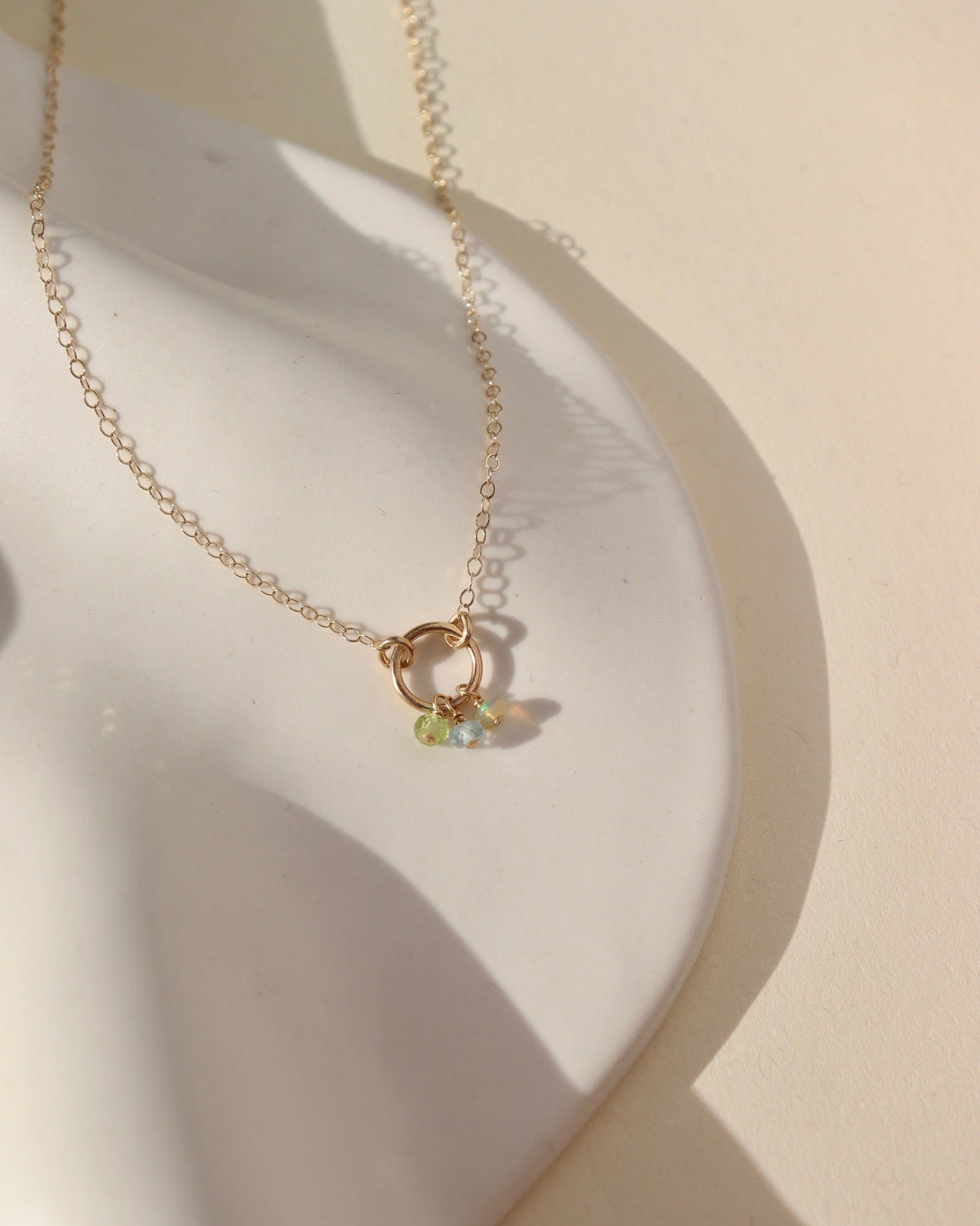 lightly hammered 14k solid gold circle pendent with dainty chain and colorful birthstone beads laid in the sunlight
