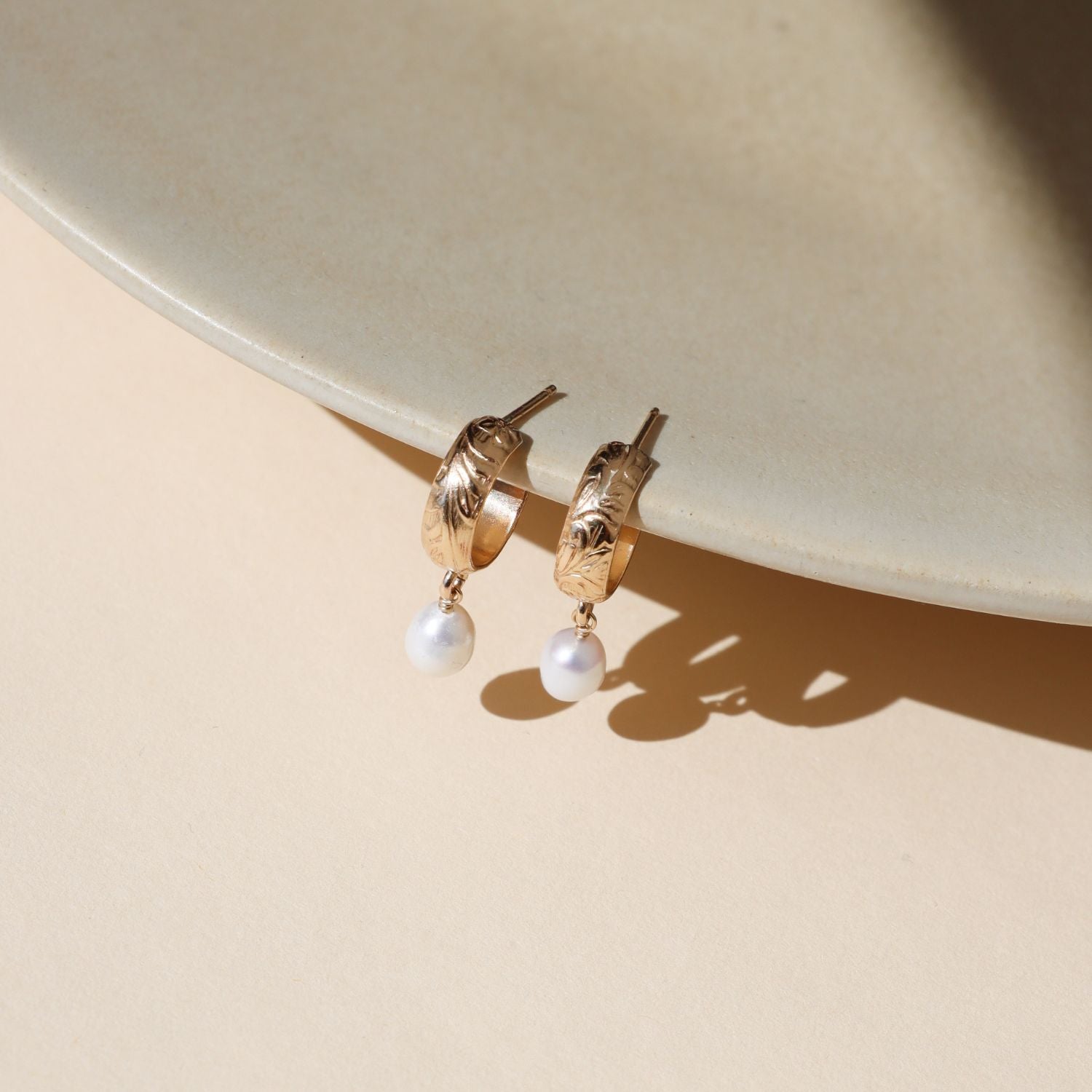 14k gold fill floral hoop studs with edison pearls dangling on a light dish