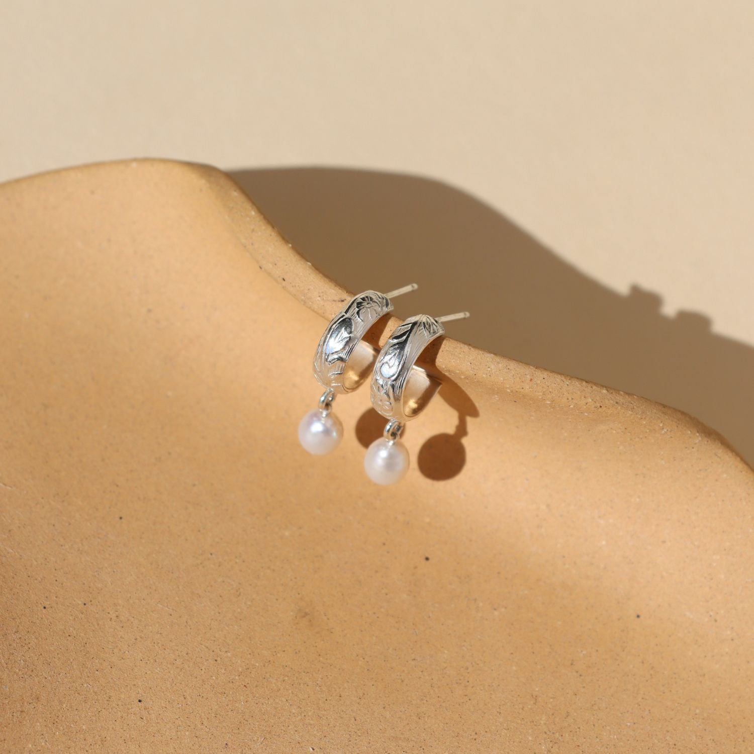 sterling silver textured hoop earrings with pearls dangling on a light dish