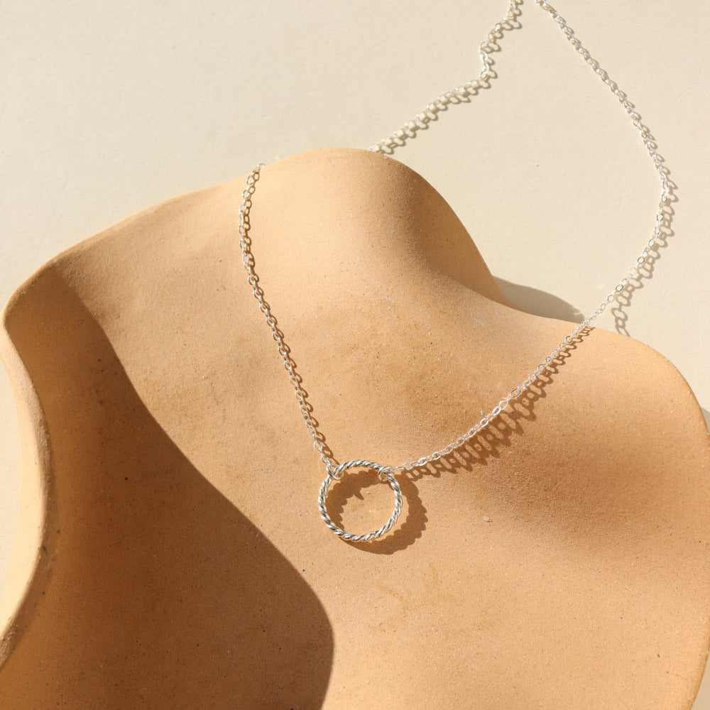 sterling silver spiral circle pendant on a a dainty sterling silver chain on a tan plate