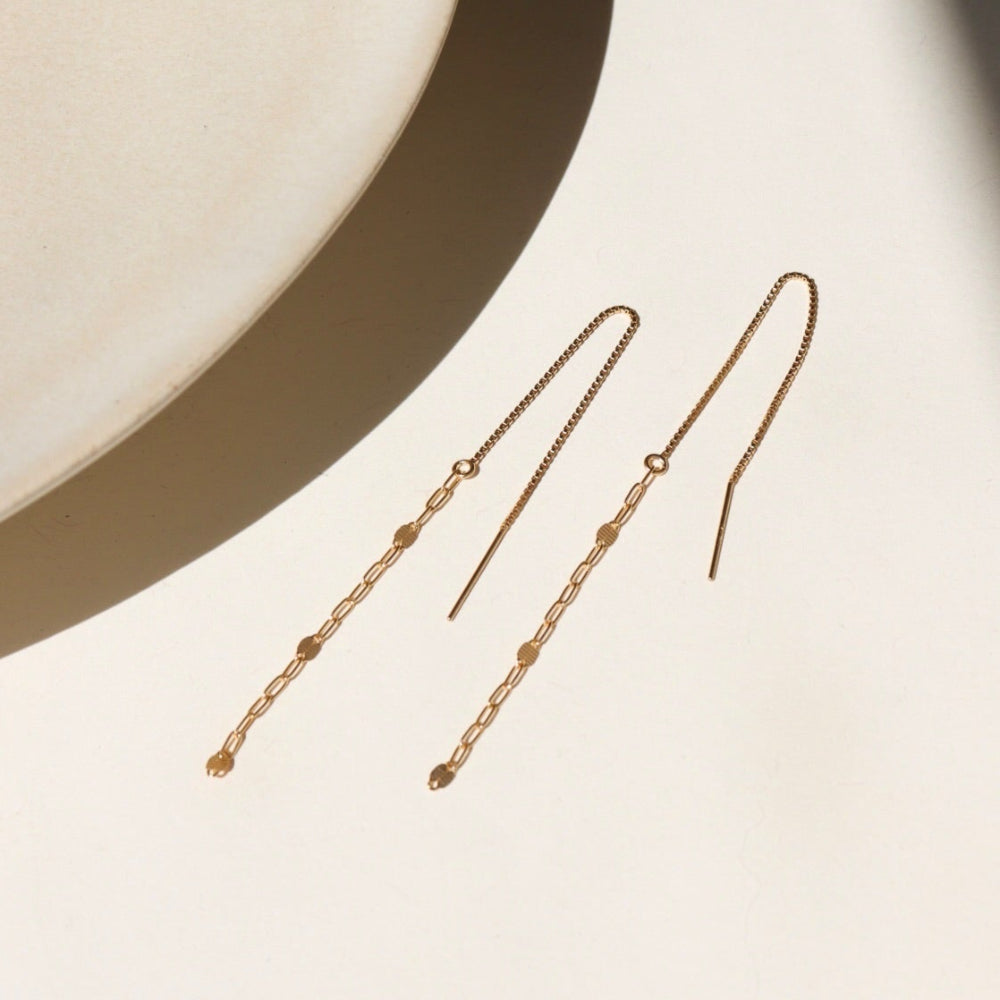 A 14k gold fill threader displayed on a cream backdrop in the sunlight 