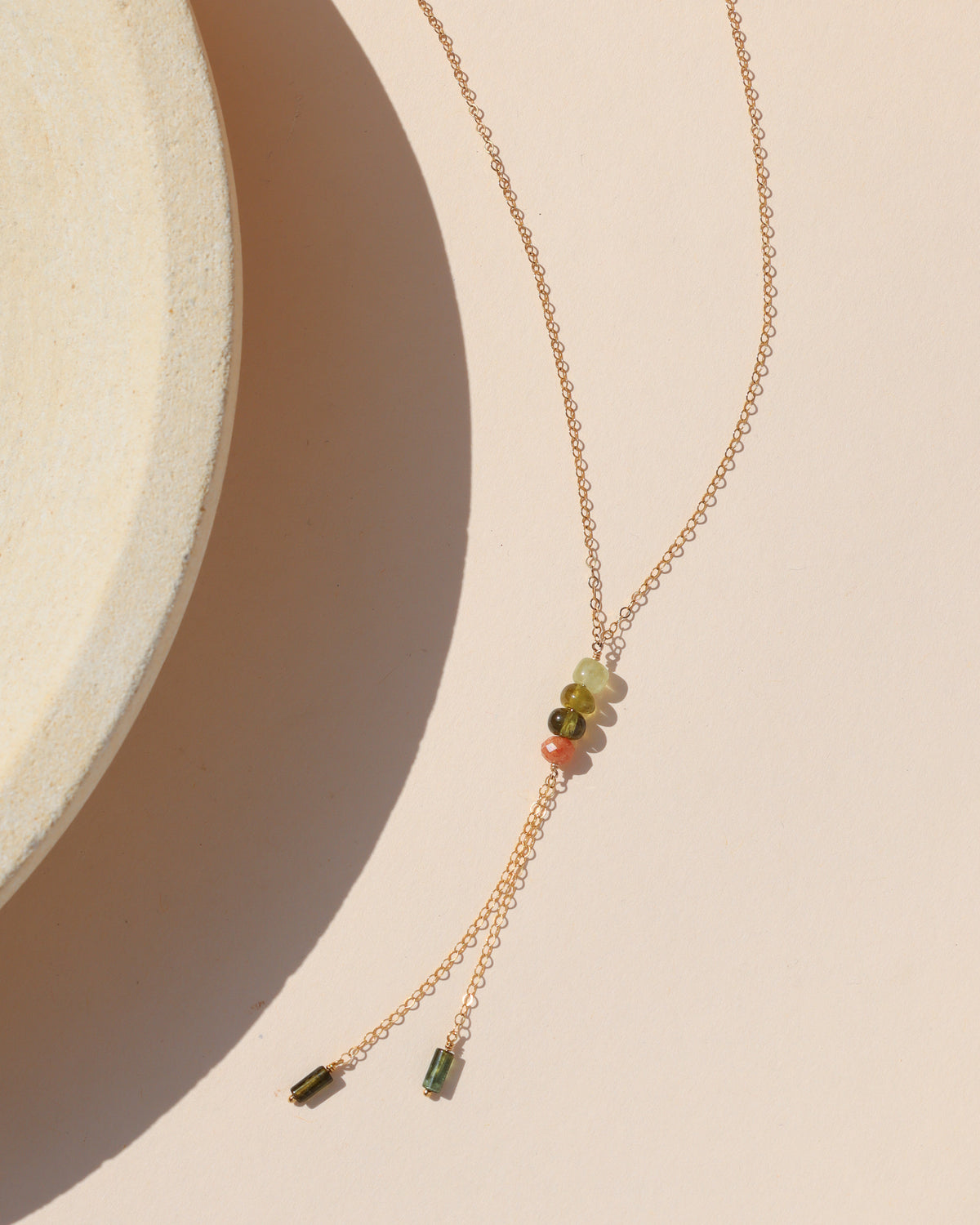Gold lariat necklace with multicolored green and coral gemstone beads and delicate chain tassels.