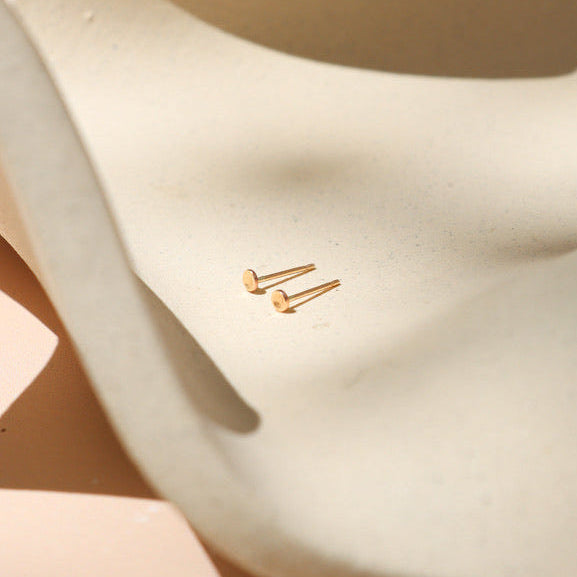 14k gold fill tiny domed circle sutds on a light dish