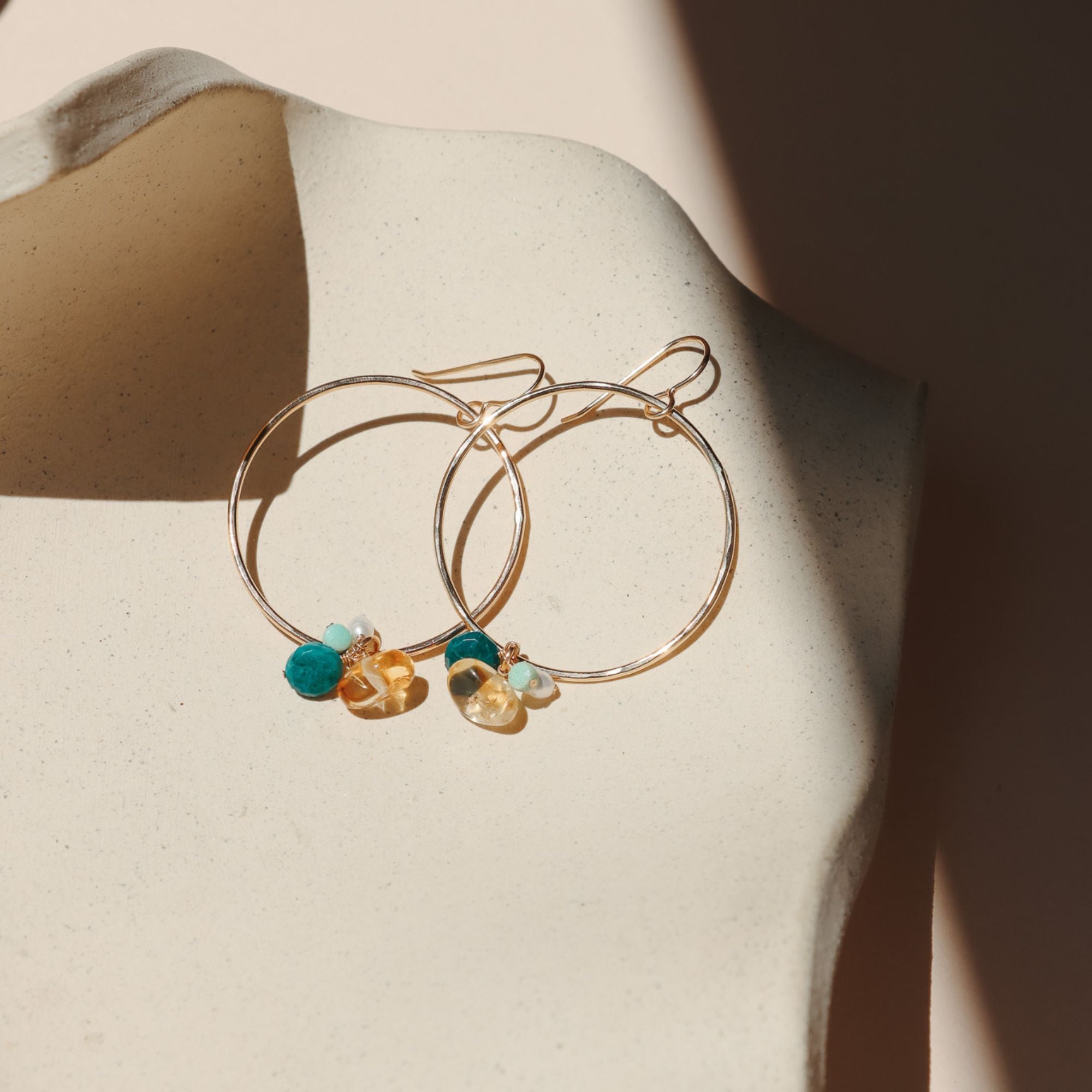 14k gold fill round hoops with gemstone drops on a light dish