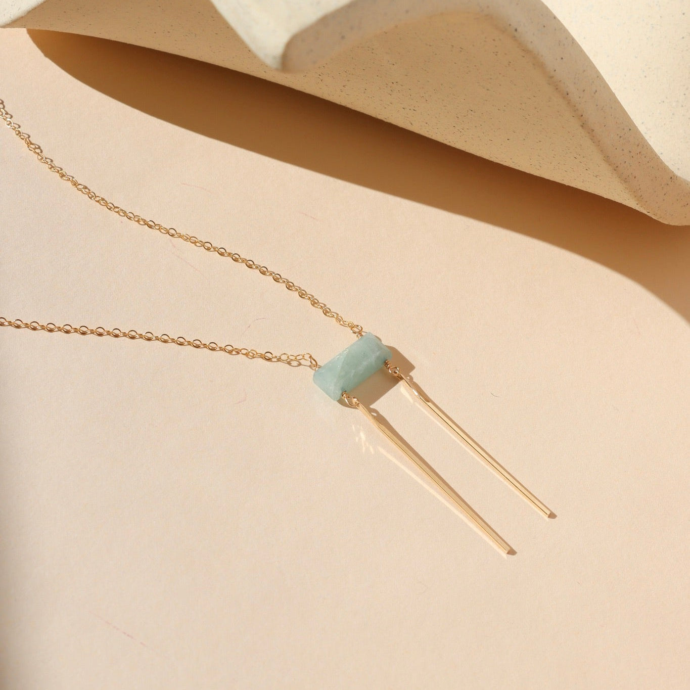 14k gold fill dainty chain necklace with rectangle aquamarine bead & 2 14k gold fill bars on a light dish
