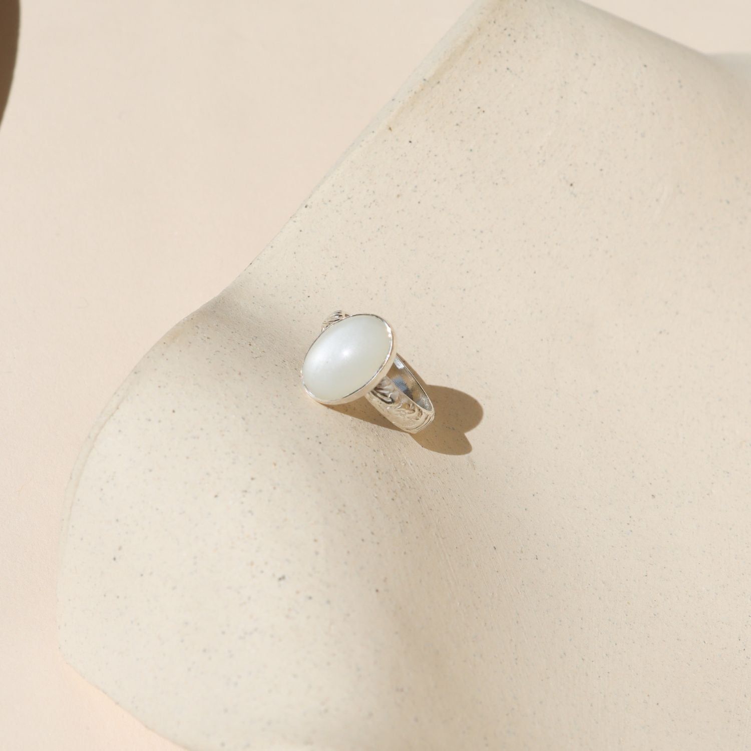 sterling silver floral band ring with oval moonstone on a light dish