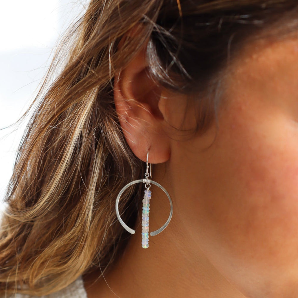 Model wearing a sterling silver hoop featuring white opal gemstones dropped 2" from earring post. 