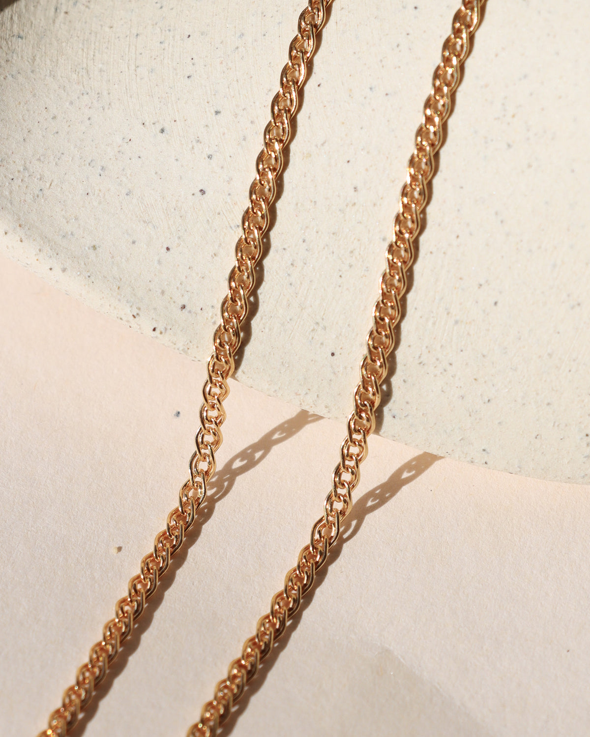 Close-up of a gold-filled woven chain necklace displayed on a neutral surface in warm sunlight.