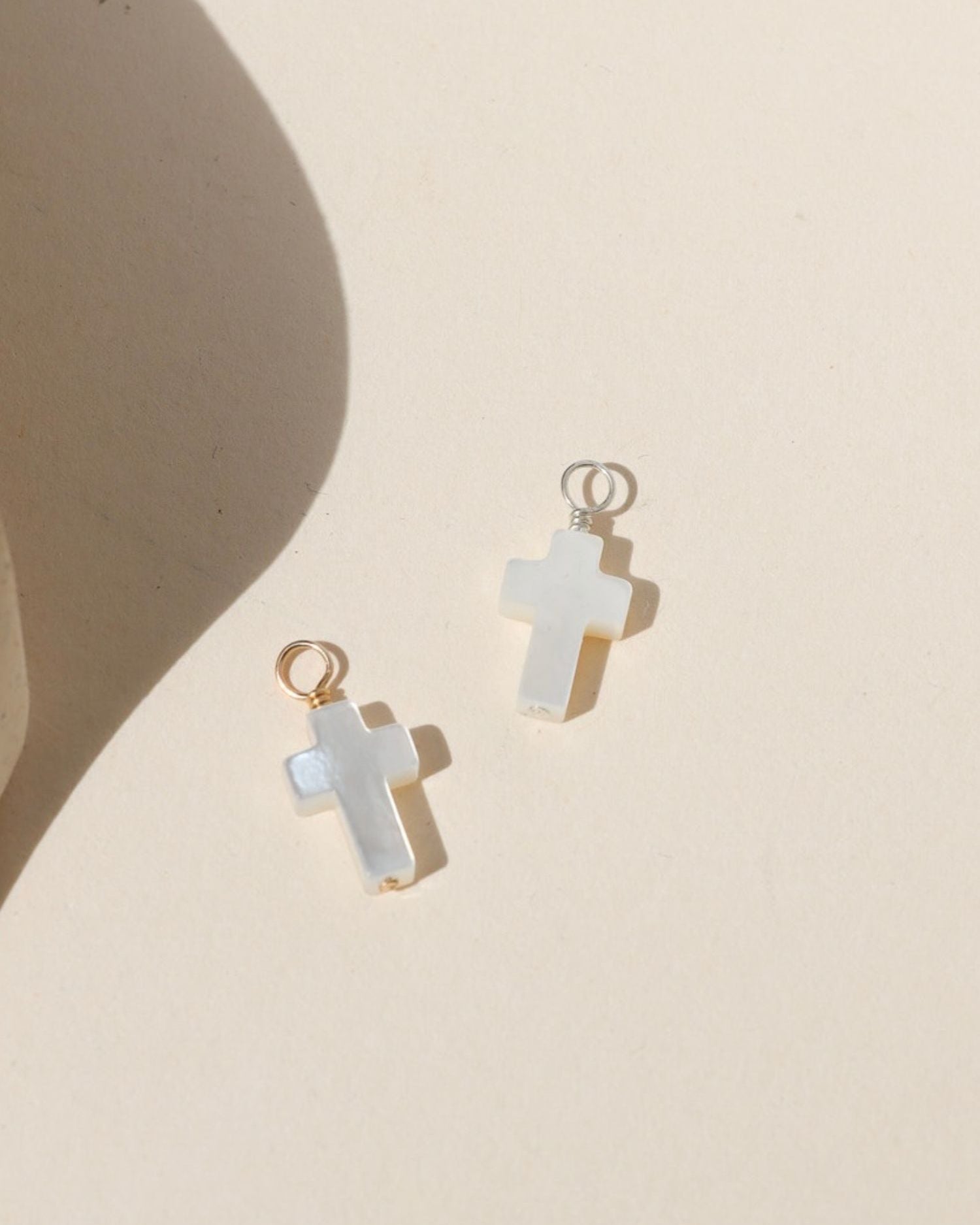 Mother of pearl cross charm with gold or silver hardware on a neutral background.