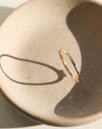 14k gold fill ring placed on a peach colored plate. The plate and ring is placed in the sunlight. This ring features a lightly hammered gold stacking ring, handmade by Token Jewelry in Eau Claire, Wisconsin