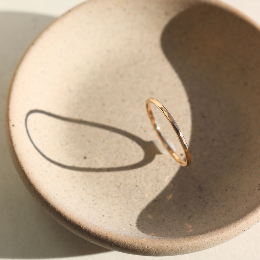 14k gold fill ring placed on a peach colored plate. The plate and ring is placed in the sunlight. This ring features a lightly hammered gold stacking ring, handmade by Token Jewelry in Eau Claire, Wisconsin