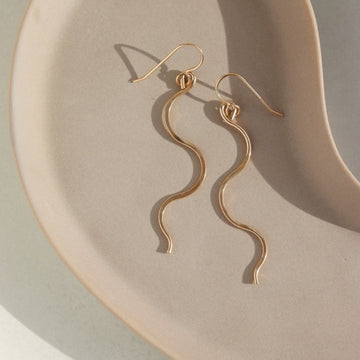 14k gold fill Sidewinder earrings placed on a tan plate. These sidewinders feature a snake like look to them with a hook earring. 