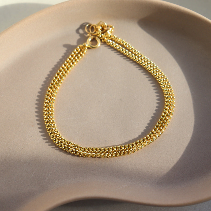 14k gold fill La Mer bracelet laid on a tan plate in the sunlight.