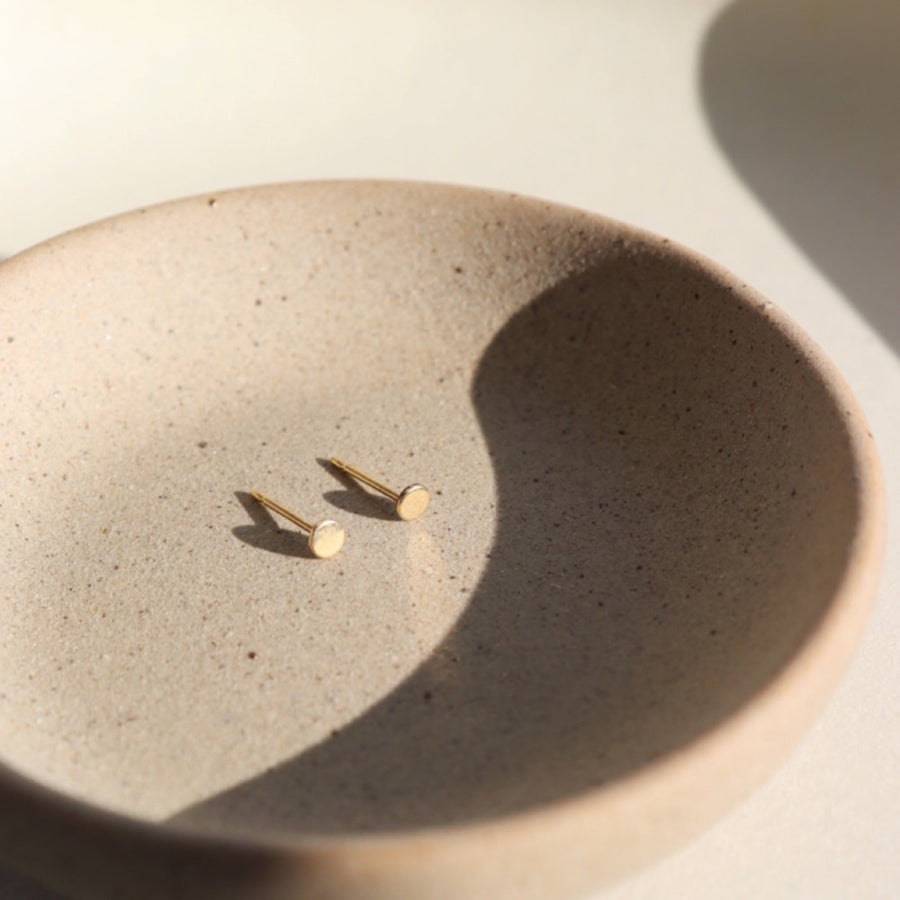tiny gold filled circle studs handmade by Token Jewelry. Earrings are displayed on a jewelry dish.