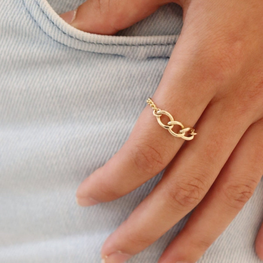 Model wearing a chain ring that features an Alexandra chain along with the la mer chain. hand is tucked into light wash jeans.