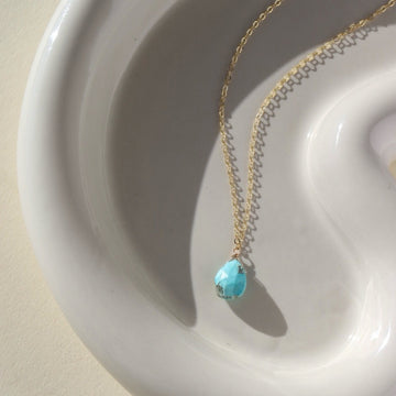 beautiful turquoise stone on a gold chain, lying on a sunlit ceramic dish
